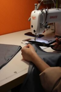 A person using scissors to cut fabric near a sewing machine, highlighting craftsmanship.